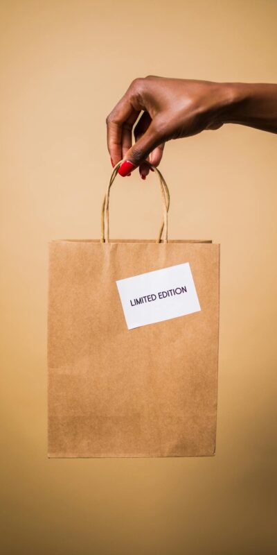 Close-up of a hand holding a brown paper shopping bag labeled 'Limited Edition' on an orange background.