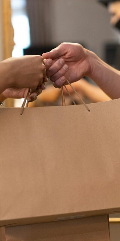 Two people exchanging a shopping bag in an indoor setting highlighting online shopping and delivery.